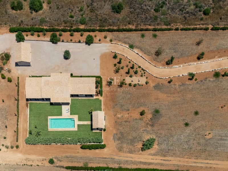 Vista aérea cenital de una villa de lujo con piscina, césped cuidado, paneles solares y amplia parcela rústica.