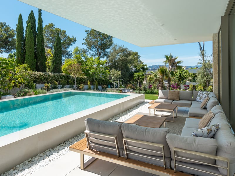 Piscine surélevée et salon de jardin gris sur une terrasse ombragée entourée d'une végétation méditerranéenne.