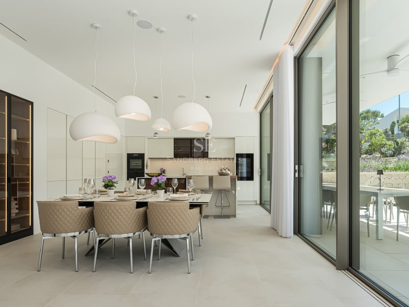 Salle à manger contemporaine avec chaises beiges, lustres design et baies vitrées ouvrant sur un jardin méditerranéen.