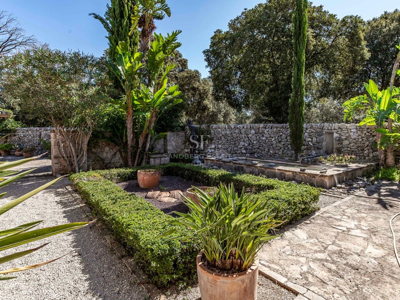 Jardin méditerranéen avec murs en pierre sèche, haies taillées, pots en terre cuite et allées de gravier.