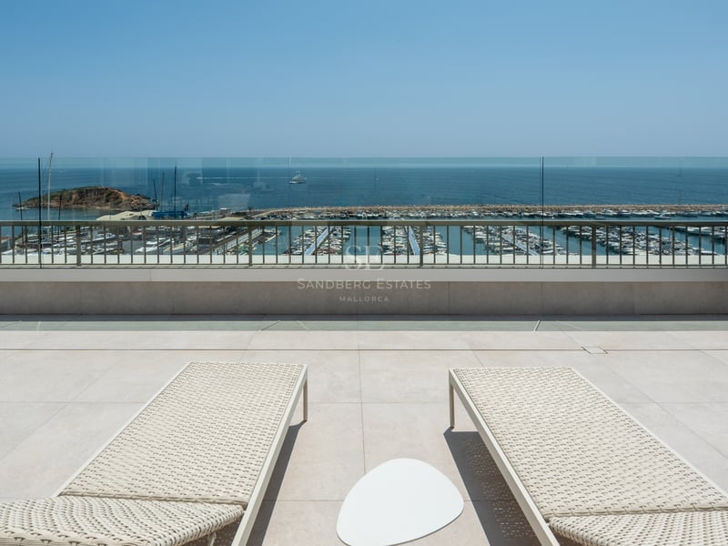Deux bains de soleil sur une terrasse en pierre surplombant un port de plaisance et la mer Méditerranée.