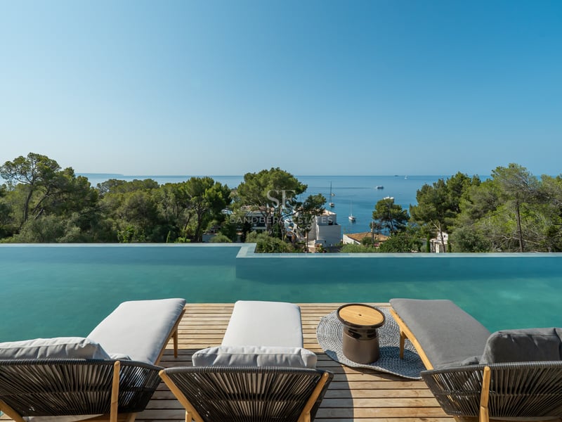 Trois chaises longues modernes sur une terrasse en bois surplombant une piscine à débordement et la mer.