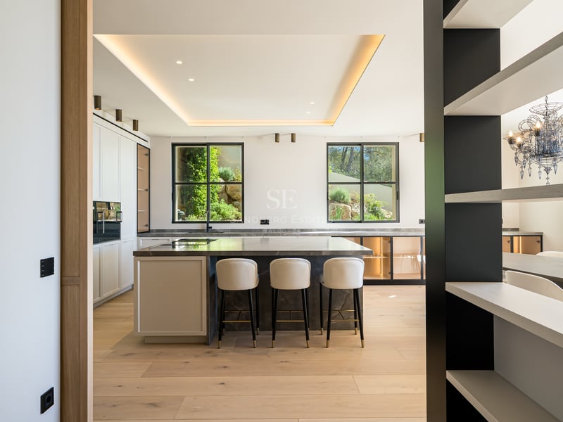 Cuisine moderne à plan ouvert avec un îlot en marbre sombre, parquet en chêne clair et fenêtres sur le jardin.