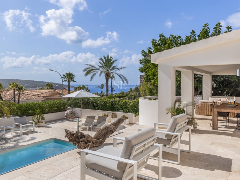 Terrasse ensoleillée avec chaises longues blanches, piscine privée et vue sur la mer sous un ciel bleu.