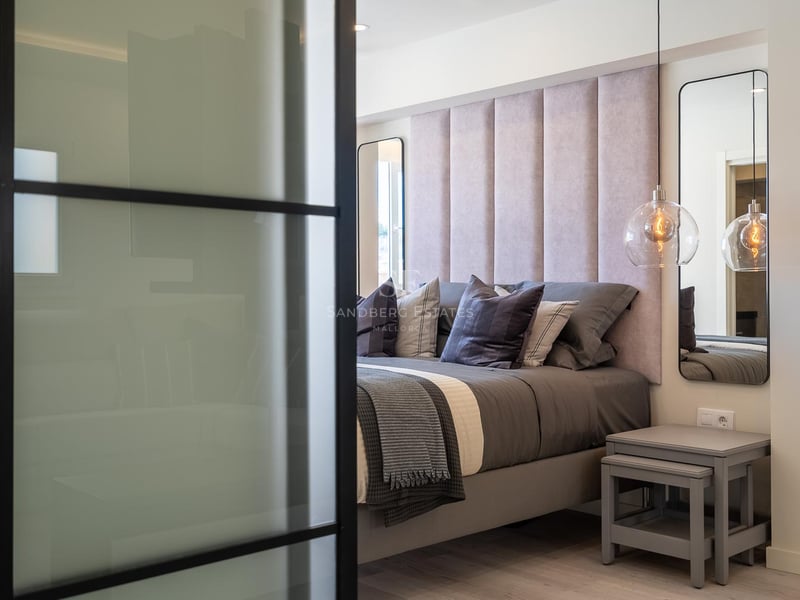Gros plan d'une chambre principale avec tête de lit capitonnée rose, suspensions en verre et cloison industrielle.