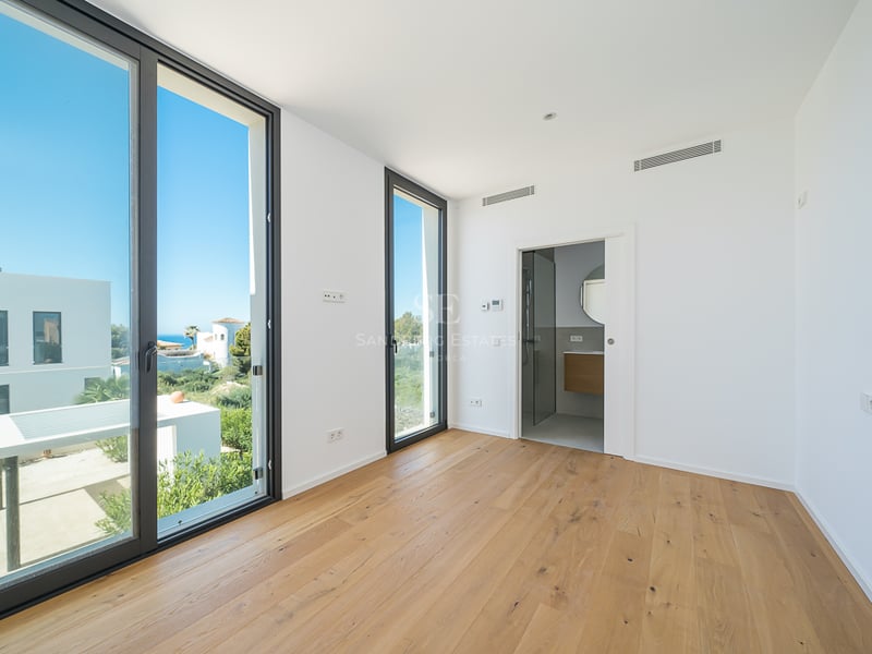 Chambre lumineuse vide avec parquet en bois clair, grandes fenêtres et accès à une salle de bain privée.