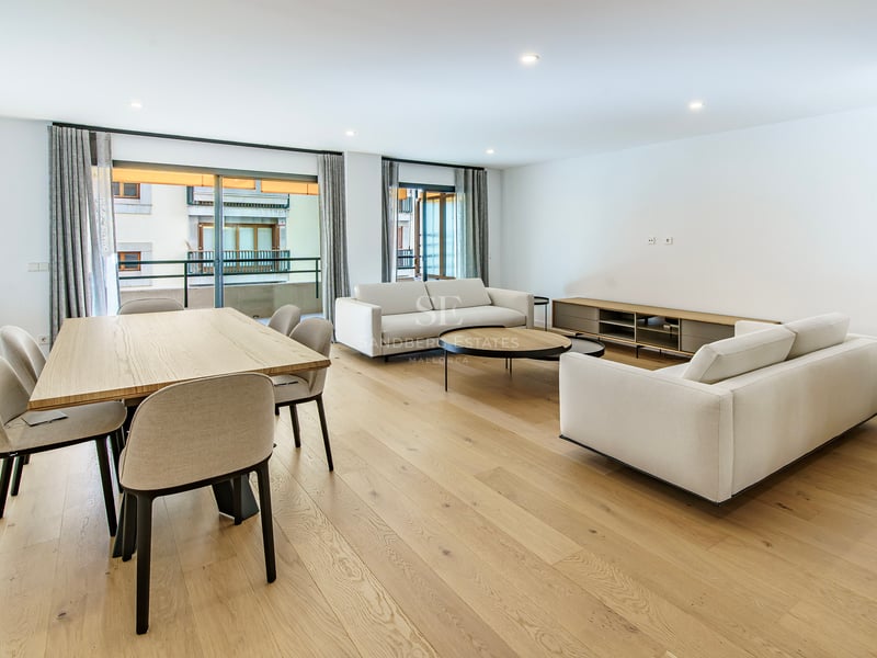 Salón abierto con sofás blancos, mesa de comedor de madera y grandes ventanales a un balcón.