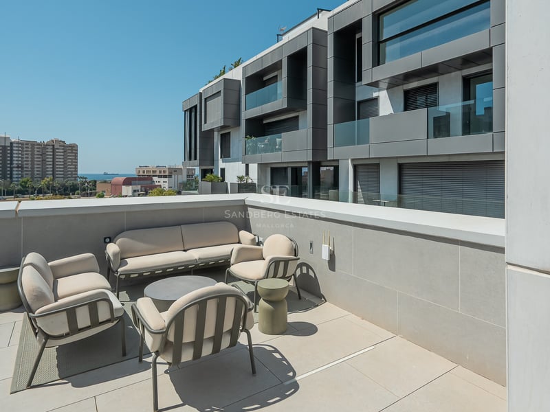 Une grande terrasse moderne avec du mobilier d'extérieur beige, un sol en carrelage gris et vue sur un bâtiment contemporain.