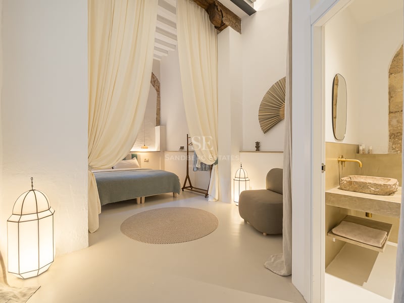Chambre élégante avec des rideaux fluides, des poutres en bois, des lanternes et une salle de bain avec vasque en pierre.
