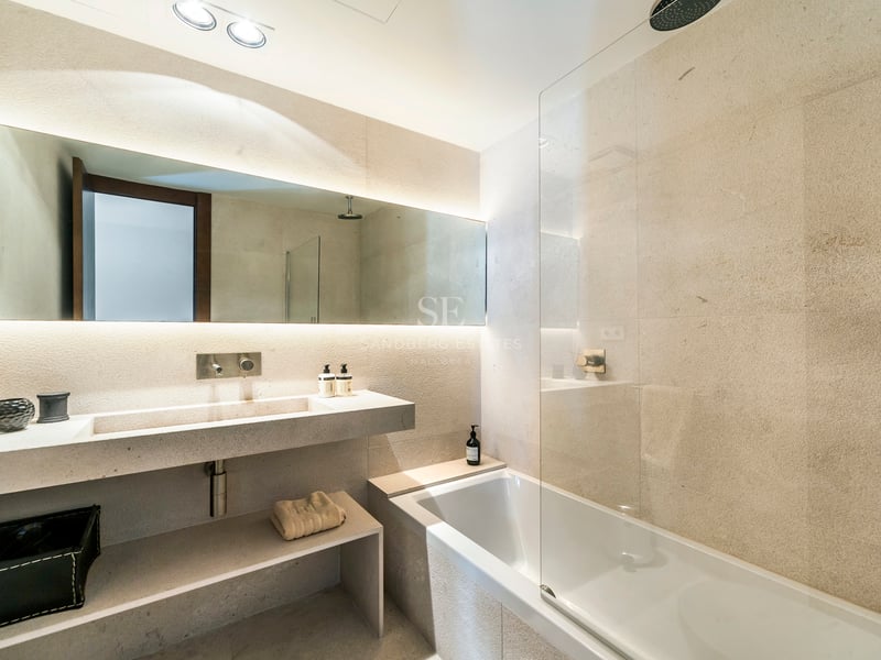 Salle de bains de luxe avec vasque en pierre, miroir rétroéclairé et baignoire avec paroi en verre.