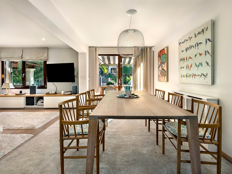 Table à manger en bois avec chaises sous une suspension sphérique, ouverte sur le salon et la terrasse.