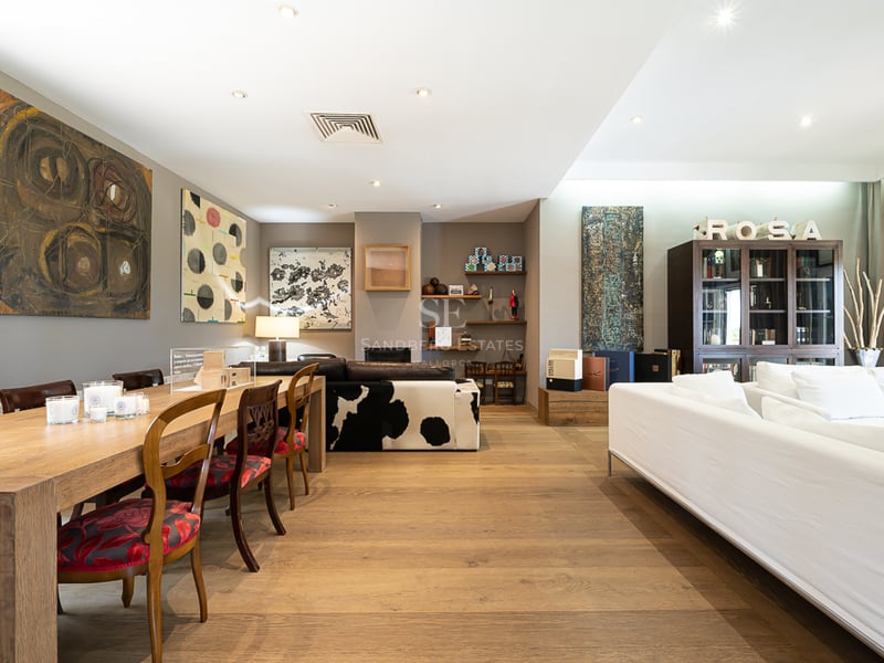 Grand salon avec parquet en chêne, art moderne, table à manger en bois et canapés blancs.