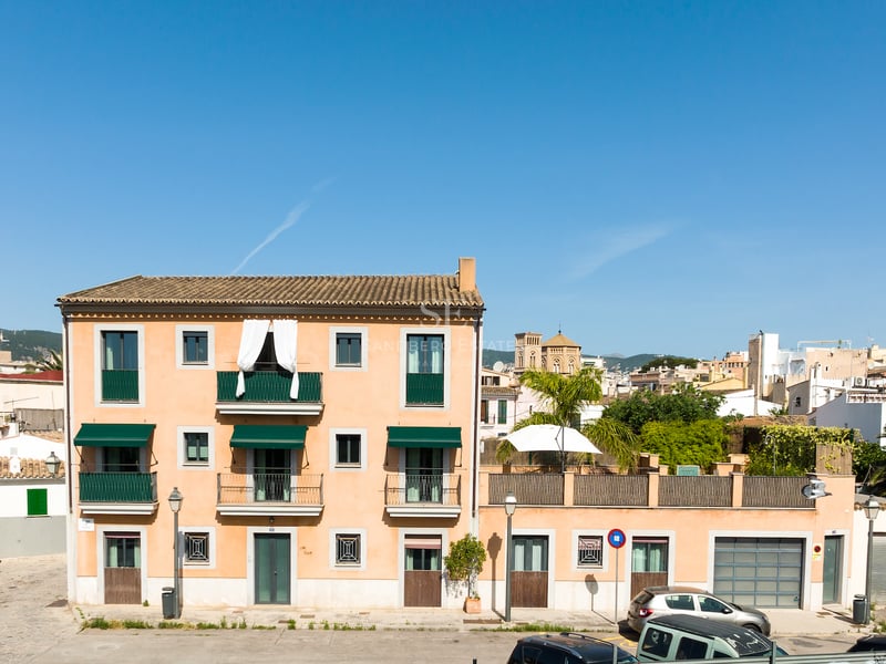 Immeuble de trois étages couleur terre cuite avec balcons et stores verts sous un ciel bleu clair.