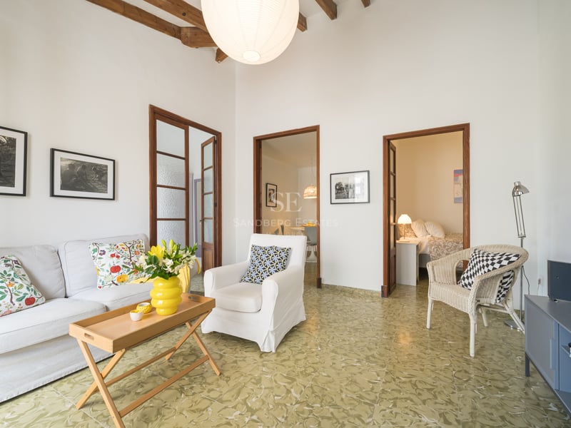 Salon lumineux avec canapé blanc, poutres en bois rustiques, carrelage vert à motifs et ouvertures vers d'autres pièces.