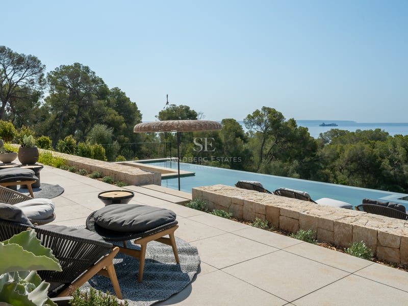 Terrasse de luxe en pierre avec piscine à débordement, salon de jardin design et vue sur la pinède et la mer.