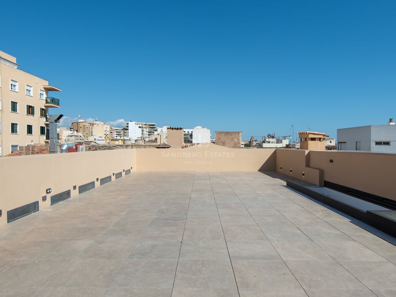Grande terrasse sur le toit avec carrelage beige et éclairage mural moderne sous un ciel bleu clair.