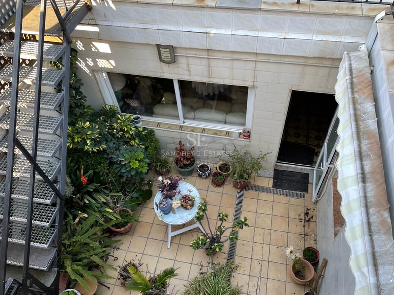 Vue d'en haut d'une terrasse carrelée avec escalier métallique, nombreuses plantes en pots et petite table ronde.