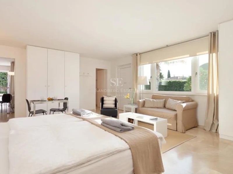 Vaste chambre parentale avec sol en marbre, coin salon, grande fenêtre sur jardin et placards blancs intégrés.