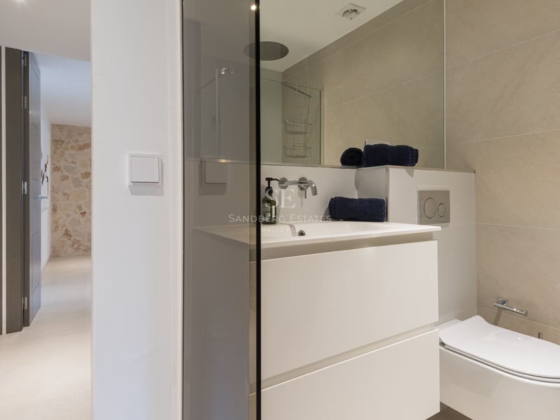 Salle de bains contemporaine avec meuble vasque suspendu blanc, douche vitrée et carrelage grand format ton sable.