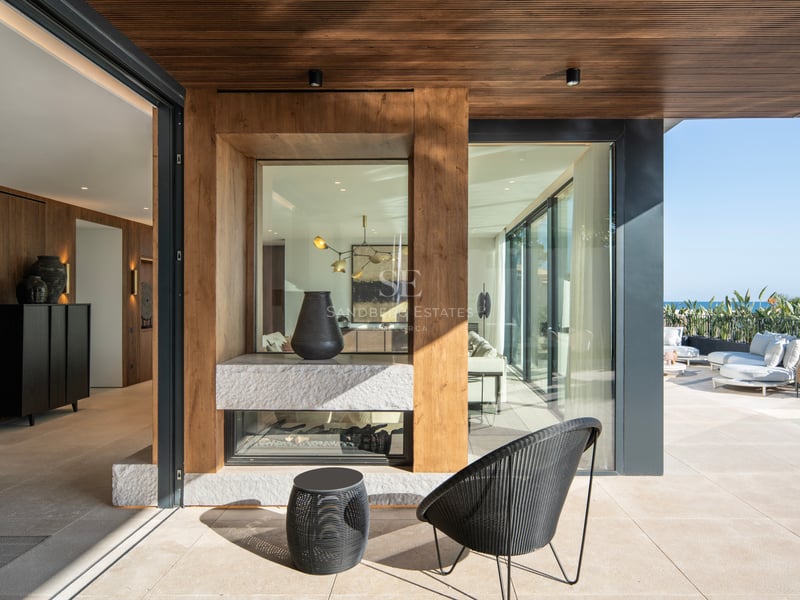 Terrasse contemporaine couverte avec cheminée en pierre double face, finitions en bois et vue sur la mer Méditerranée.