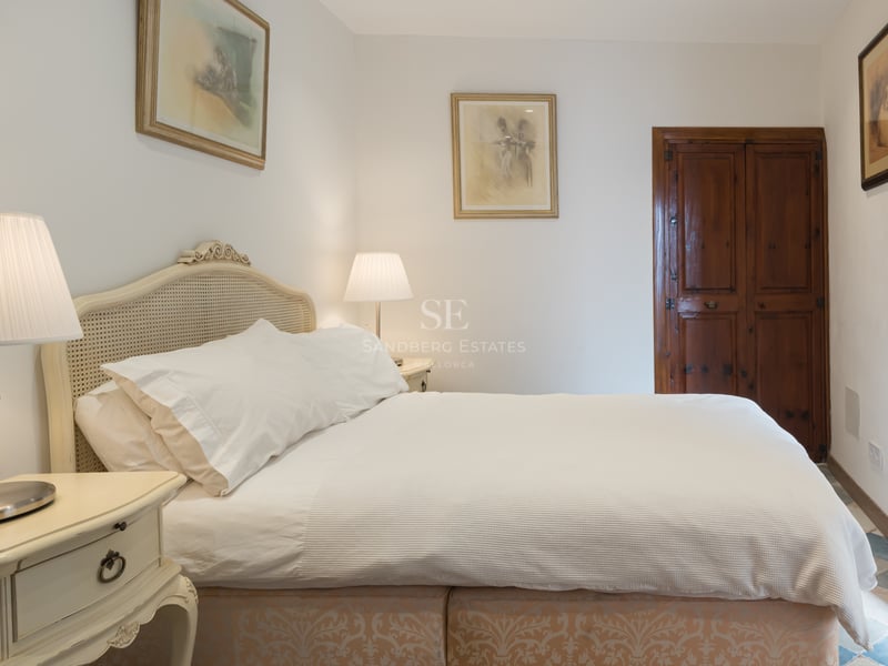 Chambre chaleureuse avec lit blanc, tête de lit en canne, lampes de chevet et porte en bois sombre.