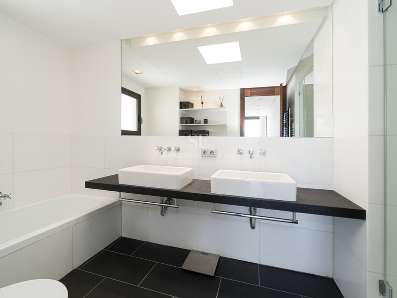 Salle de bain moderne et lumineuse avec double vasque suspendue noire, vasques blanches, grand miroir et douche vitrée.