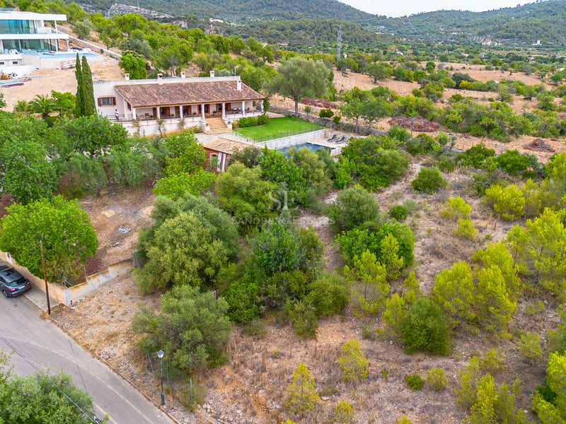 Vue aérienne d'une villa méditerranéenne rustique avec toit en terre cuite, piscine et jardin verdoyant sur les collines.