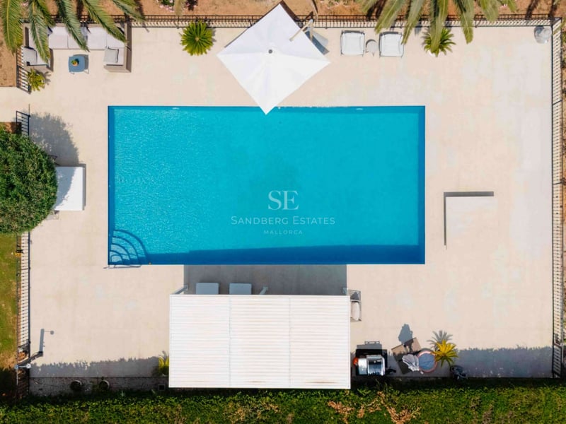 Vue aérienne d'une piscine rectangulaire turquoise entourée d'un dallage en pierre naturelle et de palmiers.