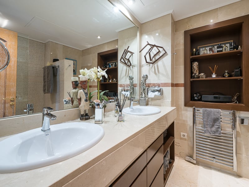 Salle de bains moderne avec deux vasques blanches, plan en marbre crème, grand miroir et étagères en bois encastrées.