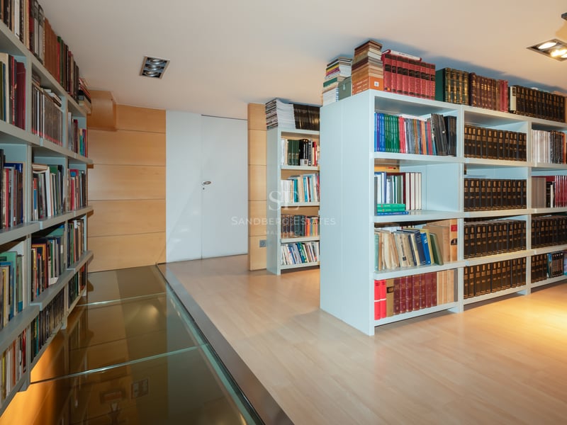 Modern home library with white floor-to-ceiling bookshelves and a transparent glass walkway over light wood flooring.