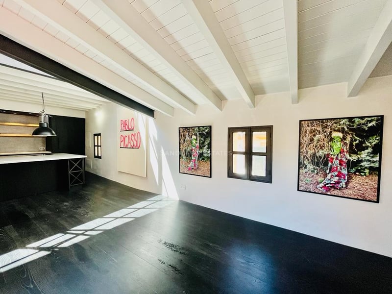 Grande pièce avec parquet sombre, plafond à poutres blanches, œuvres d'art et cuisine minimaliste.