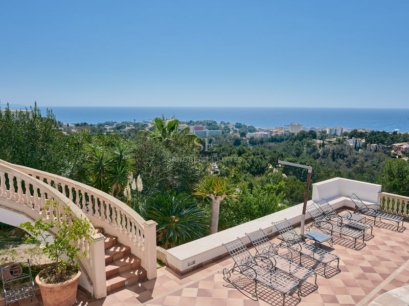 Terrasse en terre cuite avec chaises longues en fer forgé et escalier classique surplombant la mer.