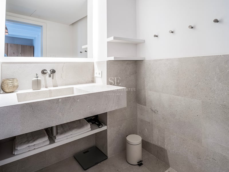Salle de bain moderne avec vanité flottante en pierre grise, lavabo intégré et grand miroir rétroéclairé.