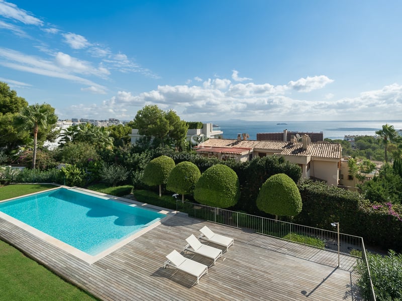 Vue en hauteur d'une piscine rectangulaire turquoise à côté d'une terrasse en bois avec des chaises longues blanches.