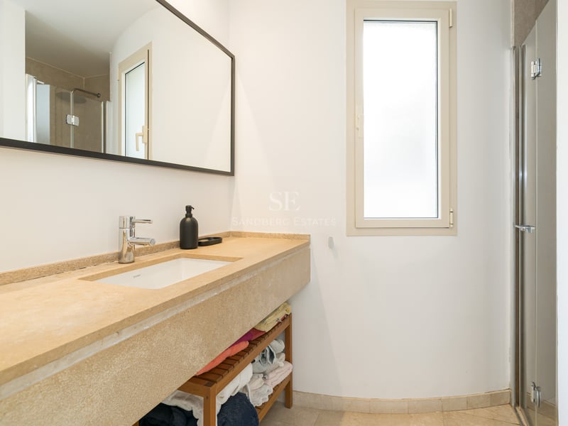 Salle de bain moderne avec lavabo en pierre beige, grand miroir et douche vitrée dans une pièce lumineuse.