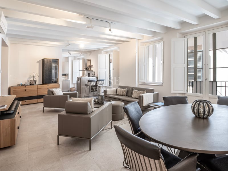 Élégant salon ouvert avec canapés gris, plafond à poutres blanches et lumière naturelle.