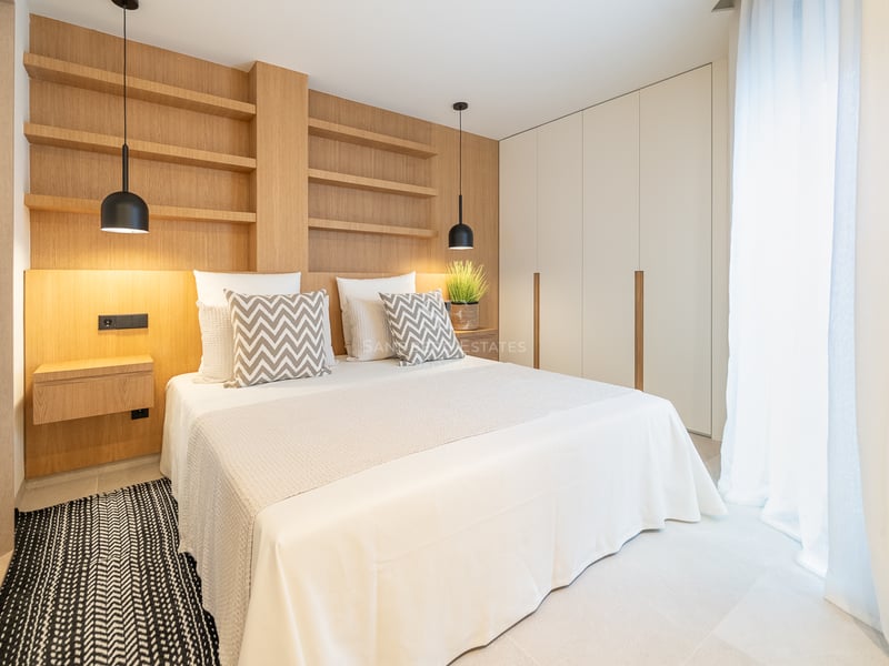 Chambre moderne avec mur en chêne clair, étagères intégrées, suspensions noires et grandes armoires blanches.