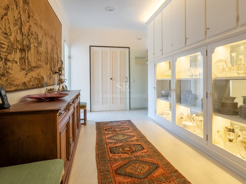 Couloir présentant une grande tapisserie historique, un tapis oriental et des vitrines blanches éclairées.