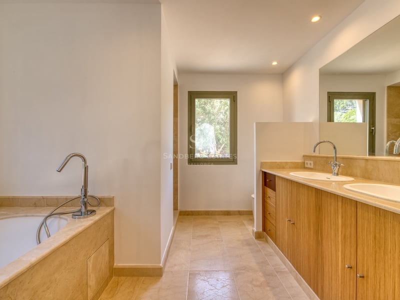 Salle de bain de luxe avec double vasque en bois, comptoirs en marbre beige, baignoire et lumière naturelle.