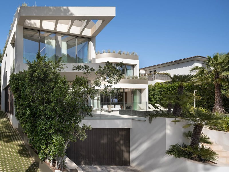 Façade d'une villa moderne blanche à plusieurs niveaux avec de grandes baies vitrées et des balcons en verre.