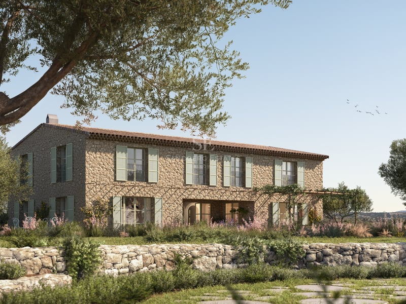 Villa en pierre à deux étages avec volets verts, entourée d'oliviers et de murets en pierre sous un ciel bleu.
