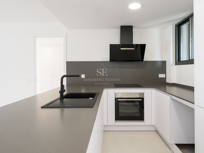 Cocina blanca impecable con encimeras de cuarzo gris, fregadero negro y electrodomésticos Bosch integrados.