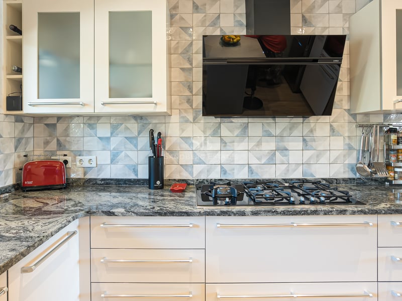 Détail d'une cuisine moderne avec plan de travail en granit, plaque de cuisson au gaz et crédence en carreaux bleus.