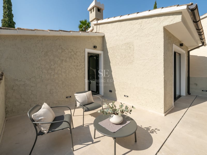 Terrasse ensoleillée avec deux chaises grises, une petite table et un sol en pierre beige.