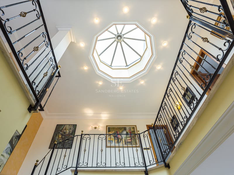 Vue vers le haut d'un grand escalier avec rampes en fer forgé et un puits de lumière octogonal au plafond.