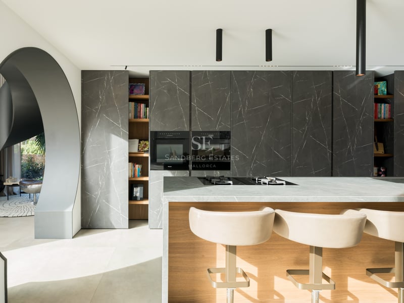 Cuisine minimaliste avec armoires en pierre sombre, îlot en bois avec tabourets blancs et appareils intégrés.