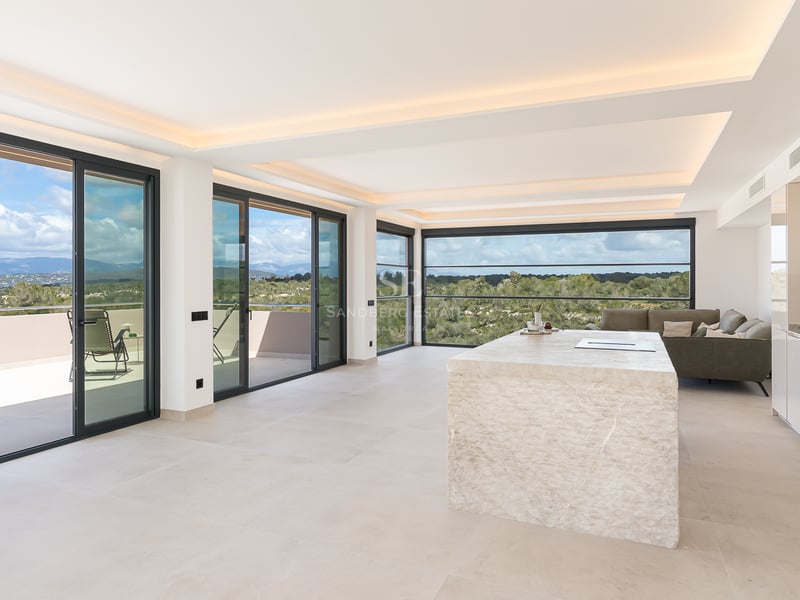 Espace de vie lumineux avec îlot en calcaire, baies vitrées toute hauteur et vue sur les montagnes.