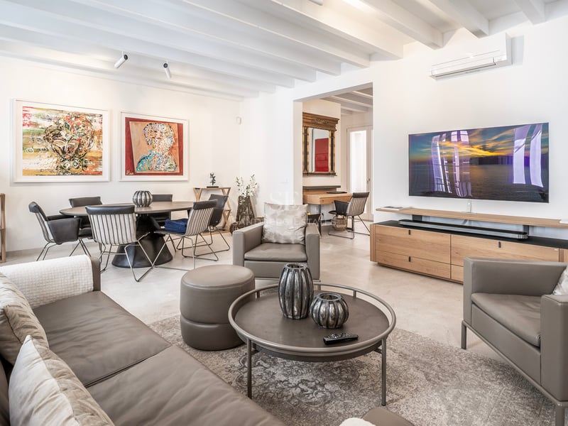 Salon moderne spacieux avec canapés en cuir gris, poutres en bois, grand téléviseur et coin repas avec œuvres d'art.