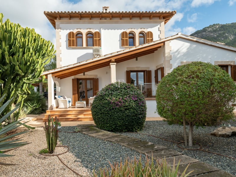 Façade de villa blanche avec volets en bois, toit en terre cuite et jardin de gravier avec cactus et agaves.