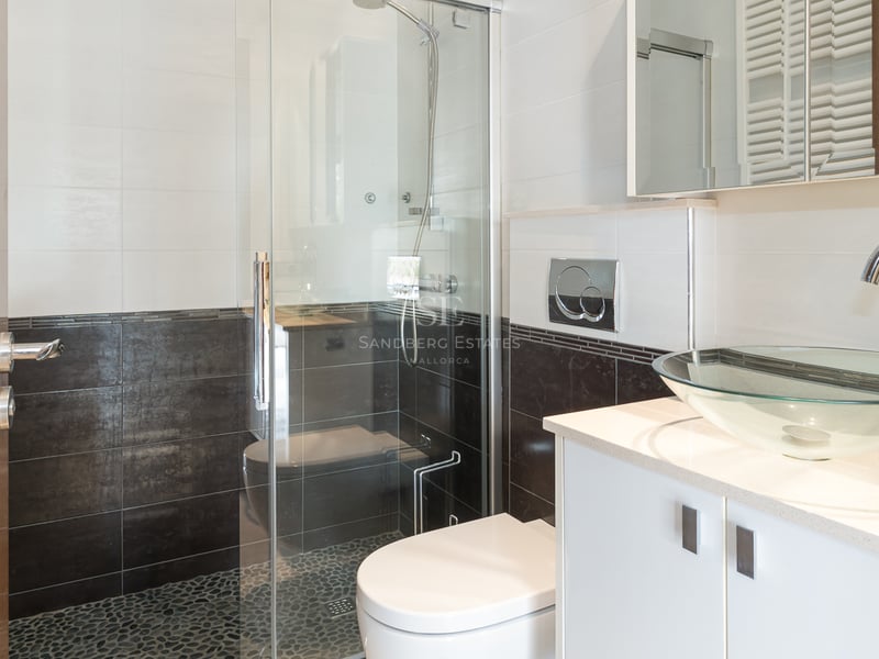 Salle de bain moderne avec vasque en verre, vanité blanche et douche vitrée avec sol en galets.